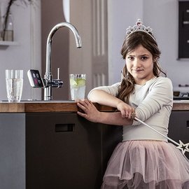 Ein verkleidetes Maedchen steht in der Kueche vor dem Trinkwasserhahn