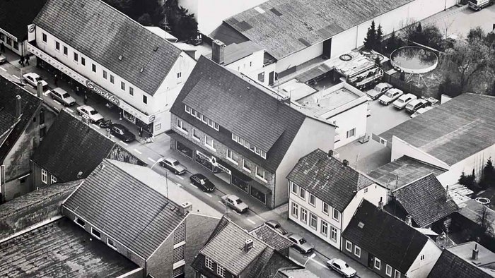 Eine Luftaufnahme einer Stadtstraße mit mehreren Autos und einem Geschäft namens 'Ceschke' im Vordergrund.