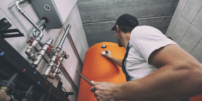 Ein Handwerker überprüft einen orangefarbenen Wassertank, während er mit einem Werkzeug in der Hand arbeitet.